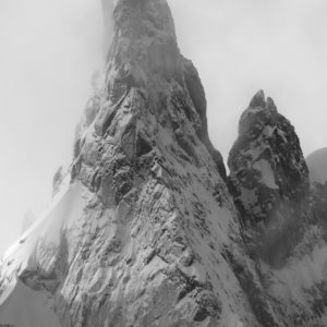 Black and white photograph of the Ago di Sciora in the Swiss Bregaglia Alps, a snow-covered rocky peak emerging from the fog after a winter storm.