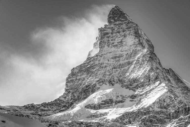 The black and white mountain top of the Matterhorn in the clouds under sunlight after a storm in the swiss alps