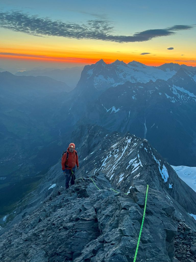 Alpiniste sur l'arête Mittellegi de l'Eiger avec lever de soleil derrière lui