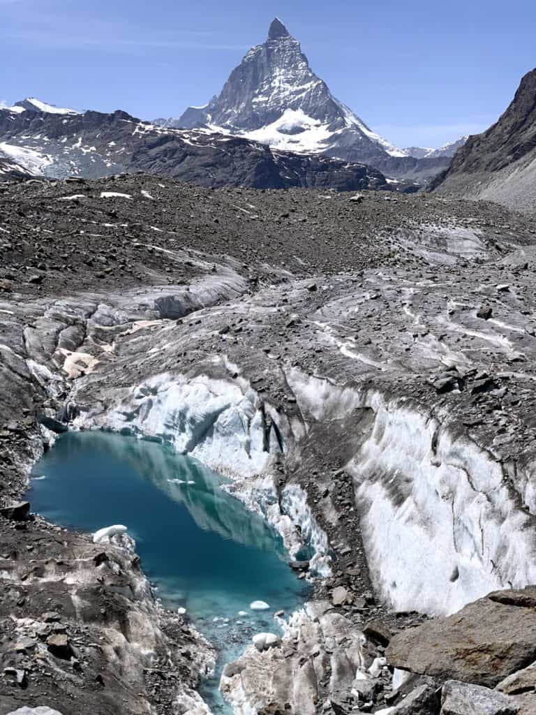 Photographie du glacier gornergletscher couvert de cailloux. Au premier plan, apparaît un lac et derrière le glacier, le mont Cervin apparaît.
