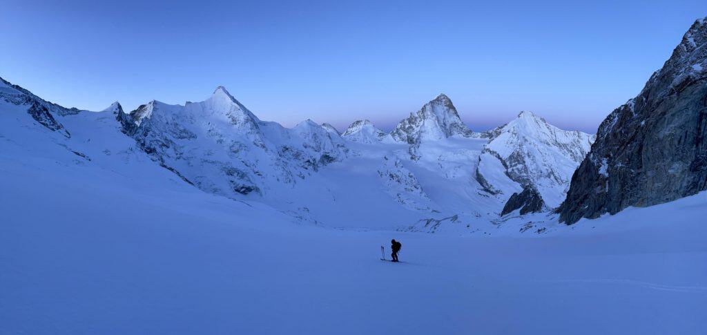 Homme seul en ski de randonnée, petit face à l'immensité des montagnes de la Couronne impériale de Zinal qui l'entourent