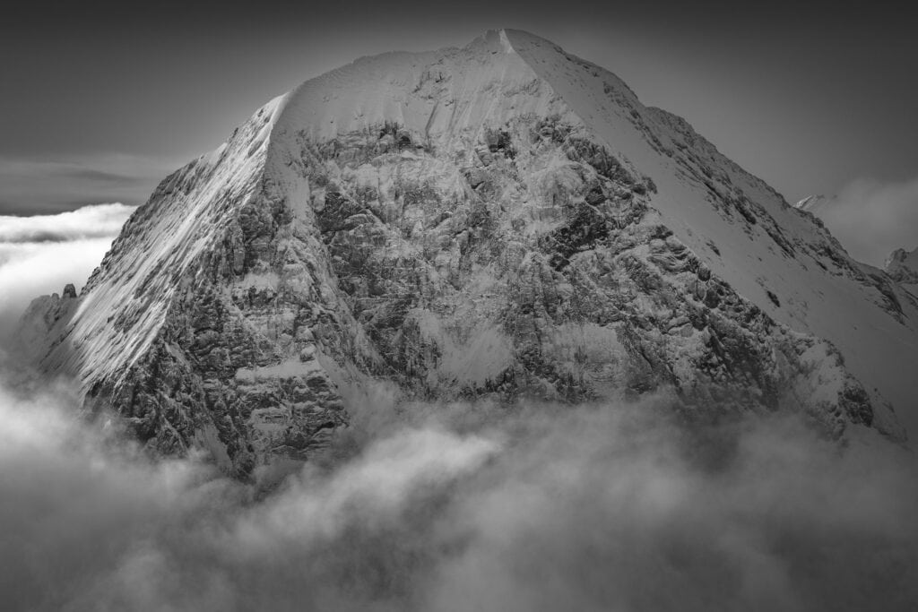 Photographie en noir et blanc de l'Eiger au-dessus d'une mer de nuages, éclairé par le soleil après une tempête - Alpes bernoises