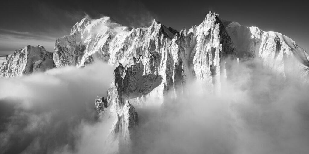 Schwarz-Weiß-Fotografie des Mont-Blanc-Massivs mit den Aiguilles du Diable, dem Grand Capucin und dem Mont Maudit, die vom Morgenlicht nach dem Sturm erleuchtet werden.