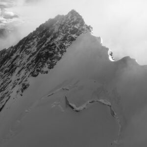 Black and white photograph of Nordend (4608 m) with illuminated crenellated ridge, surrounded by mist and clouds in the Swiss and Italian Alps.