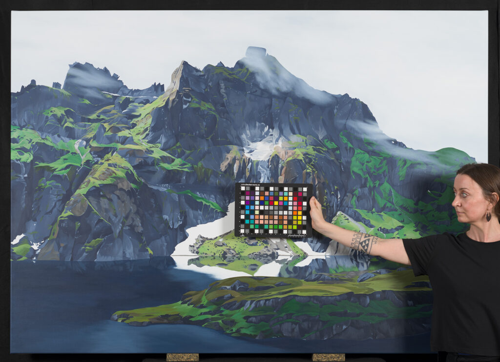 Corinne Weidmann in front of her painting of a green, craggy Alpine landscape