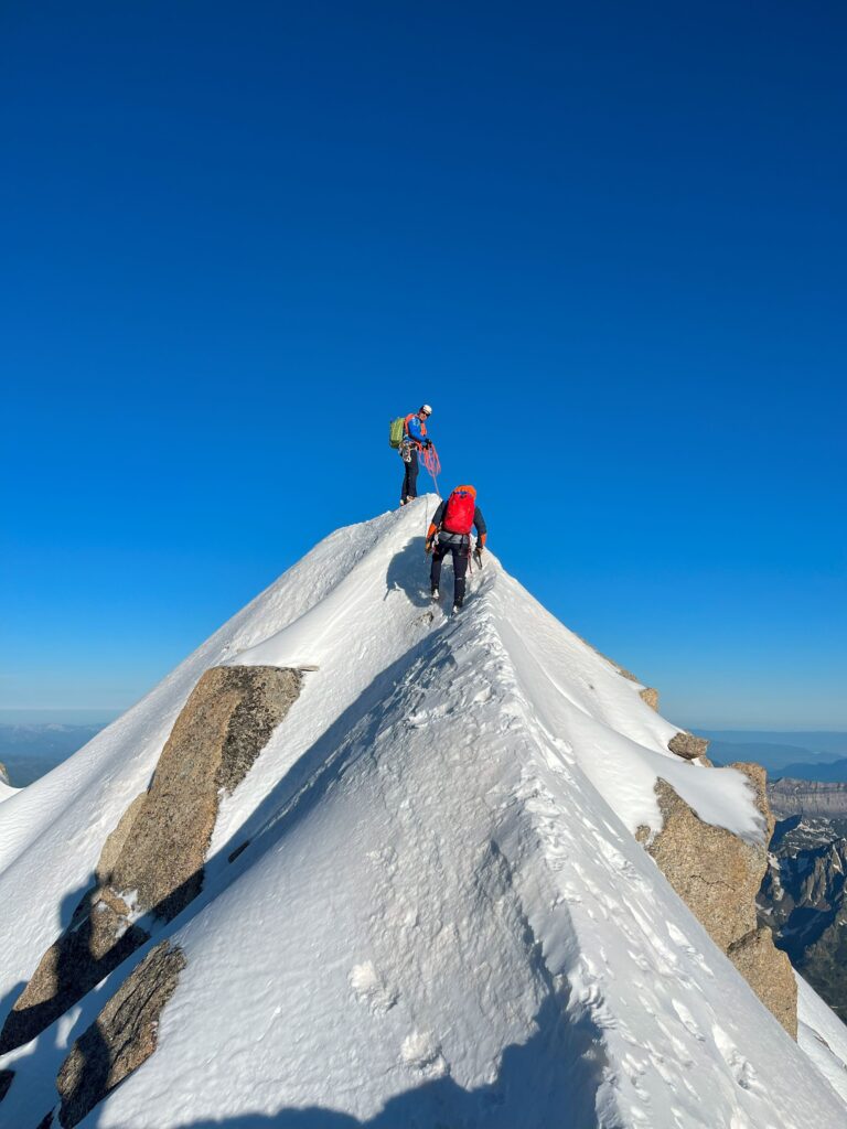 Two climbers on the snow-covered summit ridge of the Aiguille Verte, Mont Blanc massif.