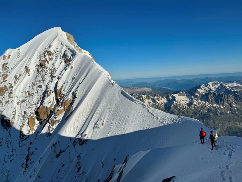 Two climbers on a snow-covered ridge during a traverse of the Aiguille Verte, Mont Blanc massif.