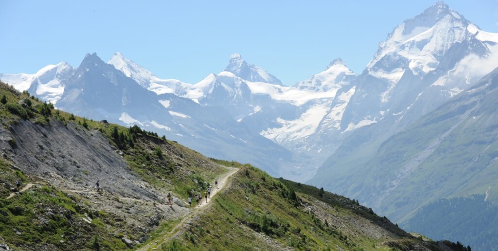 Gewundener Pfad vor Schweizer BerggipfelnEin kontemplatives Bild, das die Verbindung zwischen Laufstrecke und alpiner Erhabenheit verdeutlicht - ideal für erzählerische Zwischenspiele oder Abschnitte, die das Panorama beschreiben, das sich den Läufern bietet.