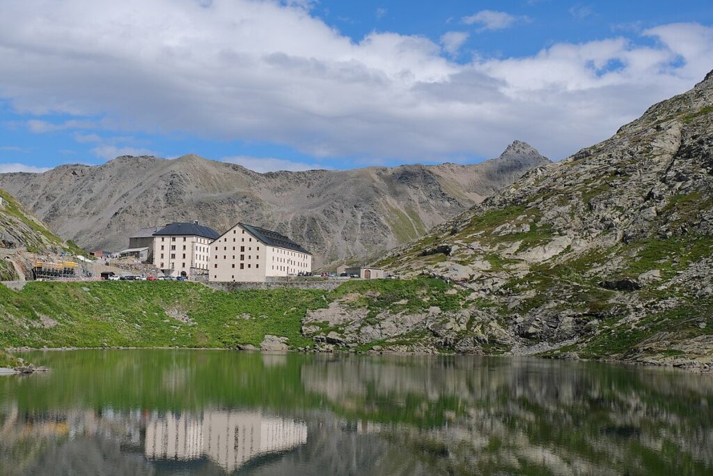 Hospice du Grand Saint Bernard devant un lac miroir et les Alpes en arrière-plan