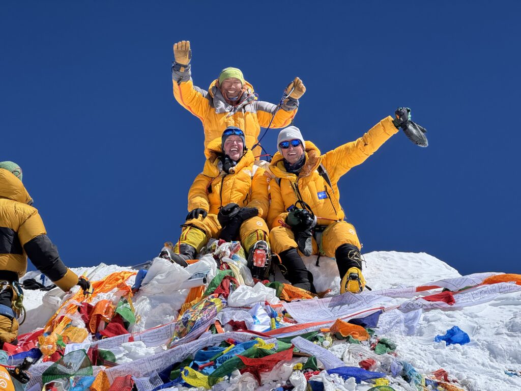 Himalajaforscher Kenton Cool, Dorjee Sherpa und ein Kunde auf dem Gipfel des Mount Everest, glücklich, mit Gebetsfahnen im Vordergrund