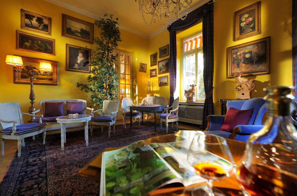 Dans la chaleur dorée du salon, chaque détail respire l’histoire : boiseries, tableaux et éclats de lumière composent un décor vivant.